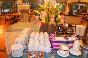 A buffet setup with stacks of plates and cups, a coffee machine, and decorative items. - Pung Waan Resort Spa (Kanchanaburi)