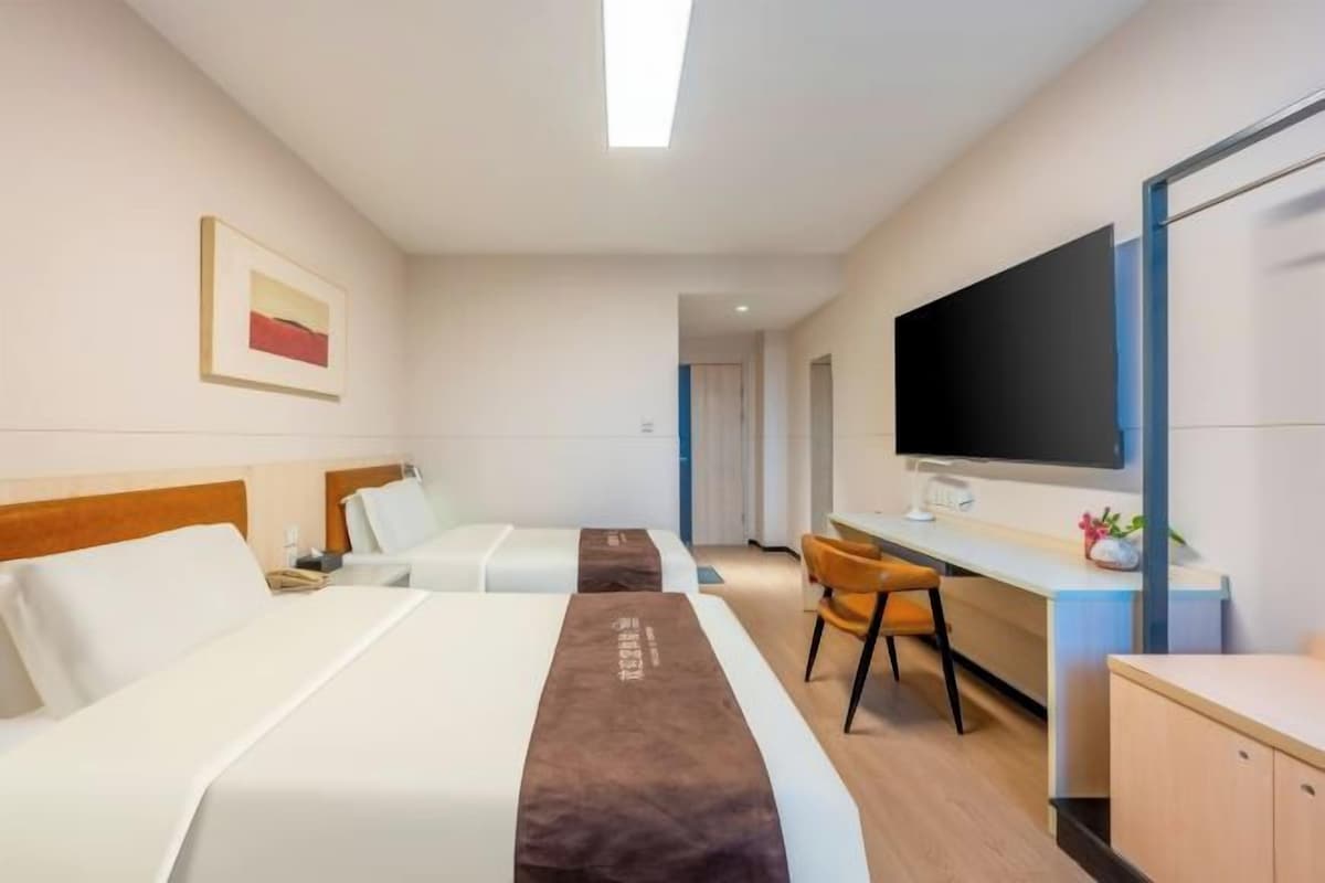 A hotel room with two beds, a desk, a chair, a TV, and a painting on the wall.