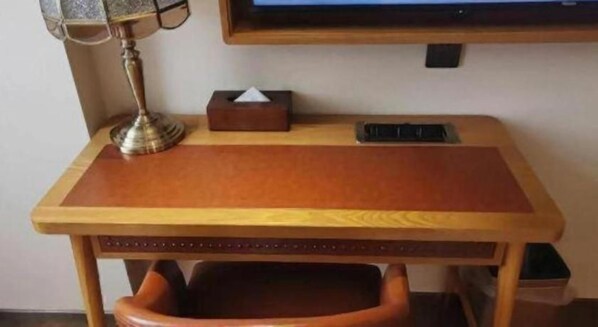 A wooden desk with a cushioned chair, a lamp, and a tissue box.