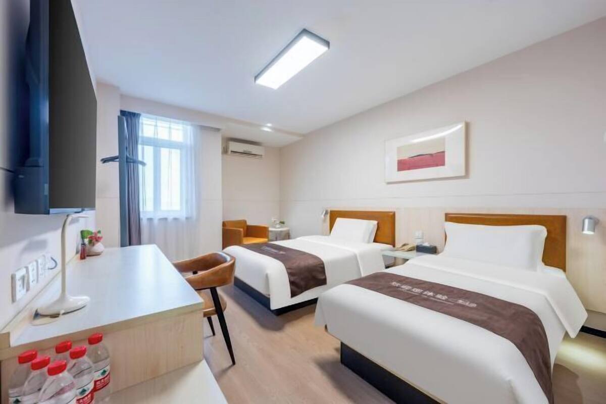 A hotel room with two beds, a desk, a TV, and a window.