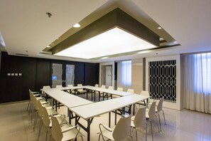 Ein Konferenzraum mit einem langen Tisch, Stühlen, einer Deckenleuchte und einem Fenster mit Vorhängen.
