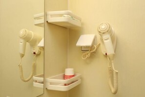 A bathroom with a hairdryer, a mirror, and a small shelf with a bottle.