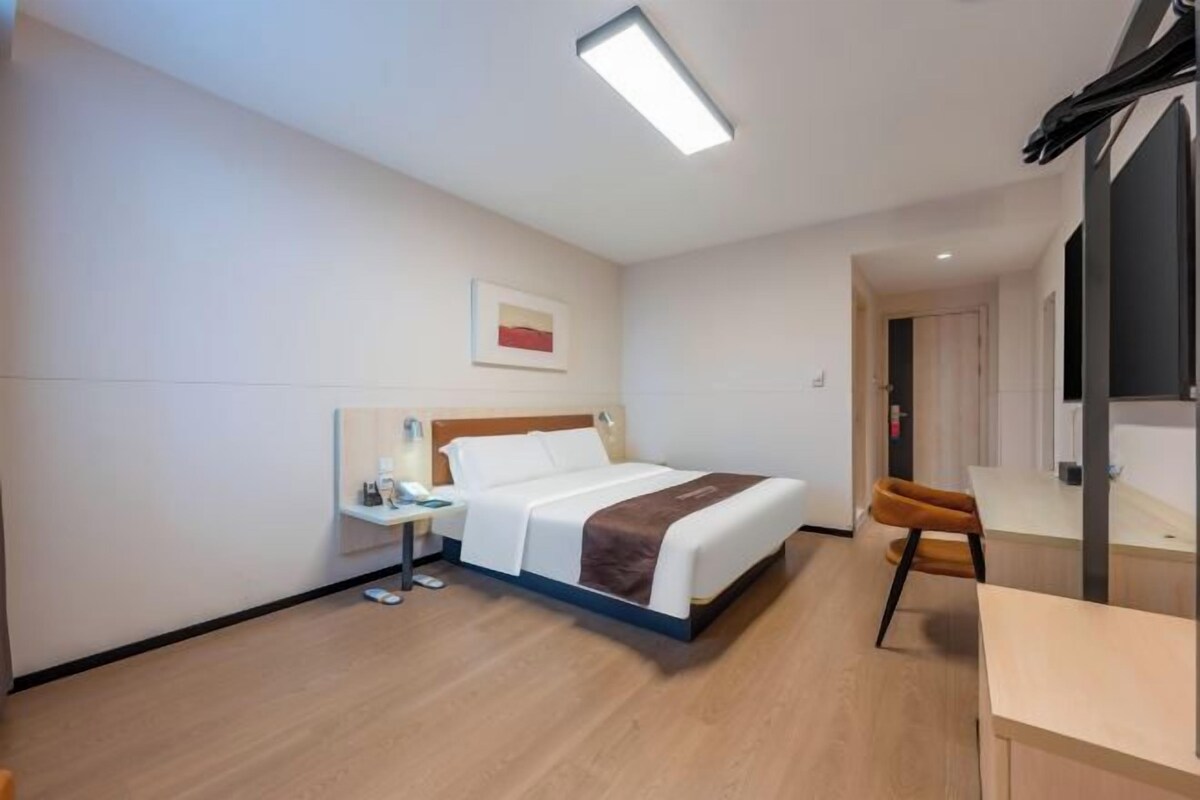 Una habitación de hotel con cama, mesita de noche, silla y un cuadro en la pared.