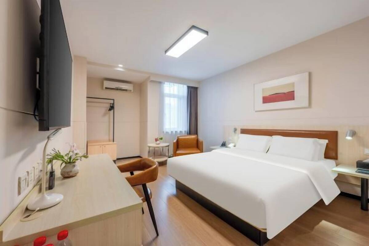 A hotel room with a bed, a desk, a chair, a TV, and a window.
