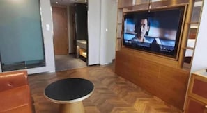 Ein Hotelzimmer mit an der Wand befestigtem Fernseher, einem runden Tisch und Holzboden.