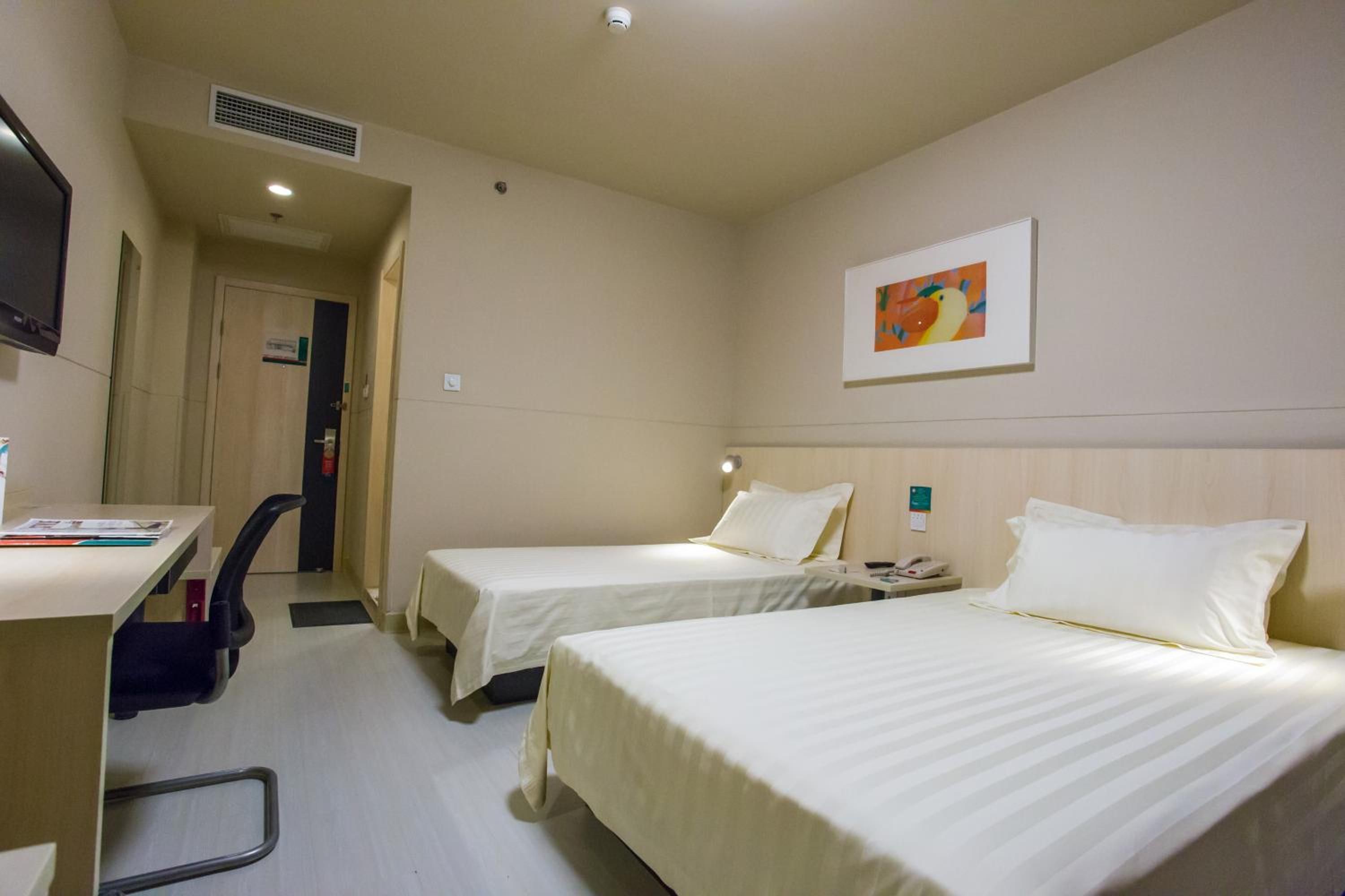 A hotel room with two beds, a desk, a chair, a telephone, and a painting on the wall.