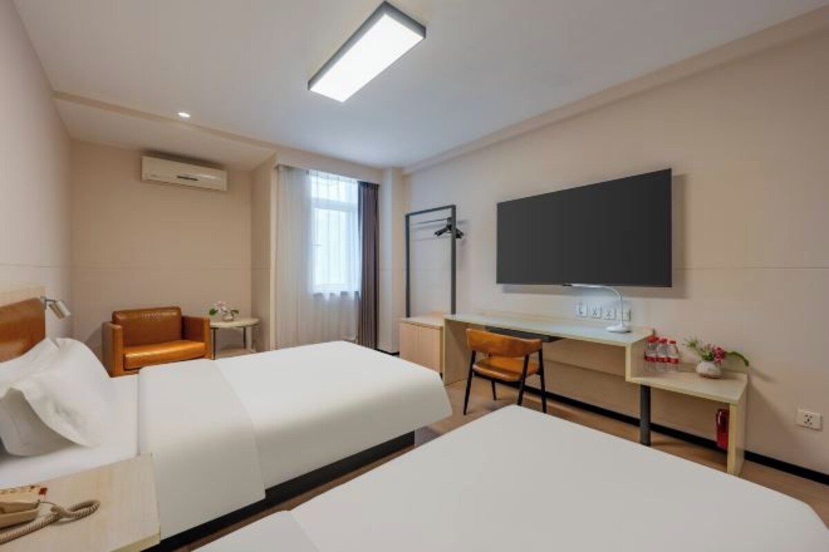 Una habitación de hotel con dos camas, un escritorio, una silla, un televisor y una ventana.