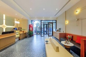 A modern hotel lobby with a reception desk, seating area, and a glass door entrance.