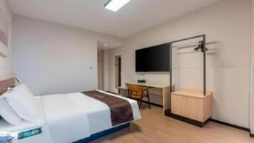 A hotel room with a bed, desk, chair, and a TV mounted on the wall.