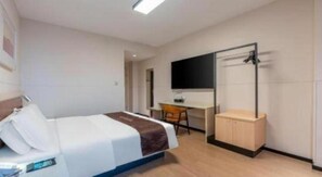Ein Hotelzimmer mit Bett, Schreibtisch, Stuhl und einem an der Wand befestigten Fernseher.