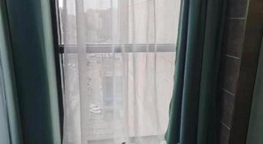 A window with sheer curtains, a view of buildings outside, and a tiled wall to the right. - Jinjiang Inn (Tianjin South Railway Station) (Tianjin)