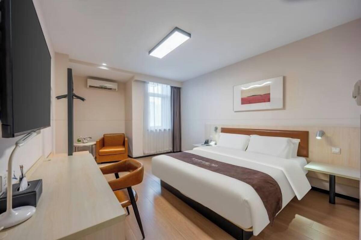 A hotel room with a bed, a desk, a chair, a TV, and a window.