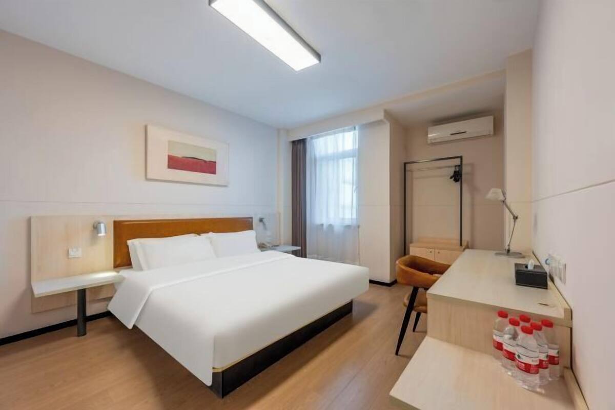 A hotel room with a bed, bedside table, chair, desk, and a water dispenser.