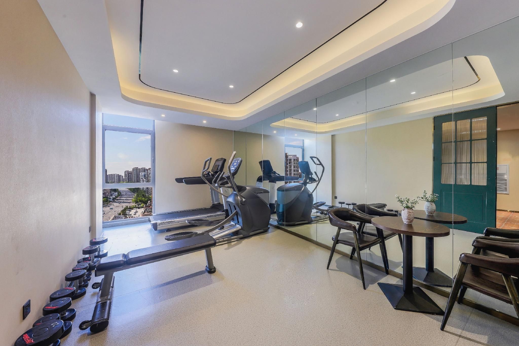 Une salle de sport moderne équipée de machines de cardio, de postes d’entraînement en musculation et offrant une vue sur la ville.
