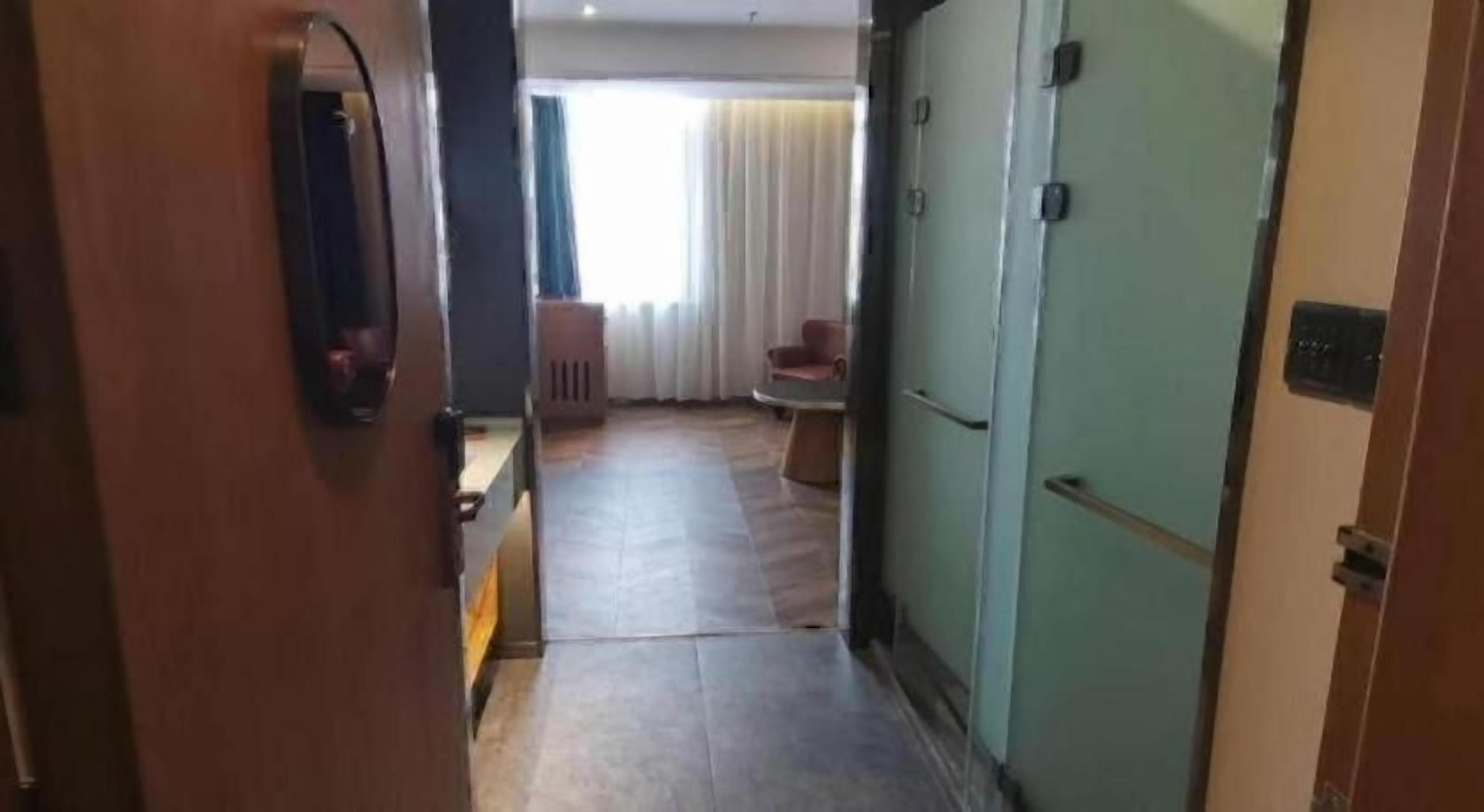A hotel hallway with a wooden door, a green wall, and a seating area with a table and chairs.