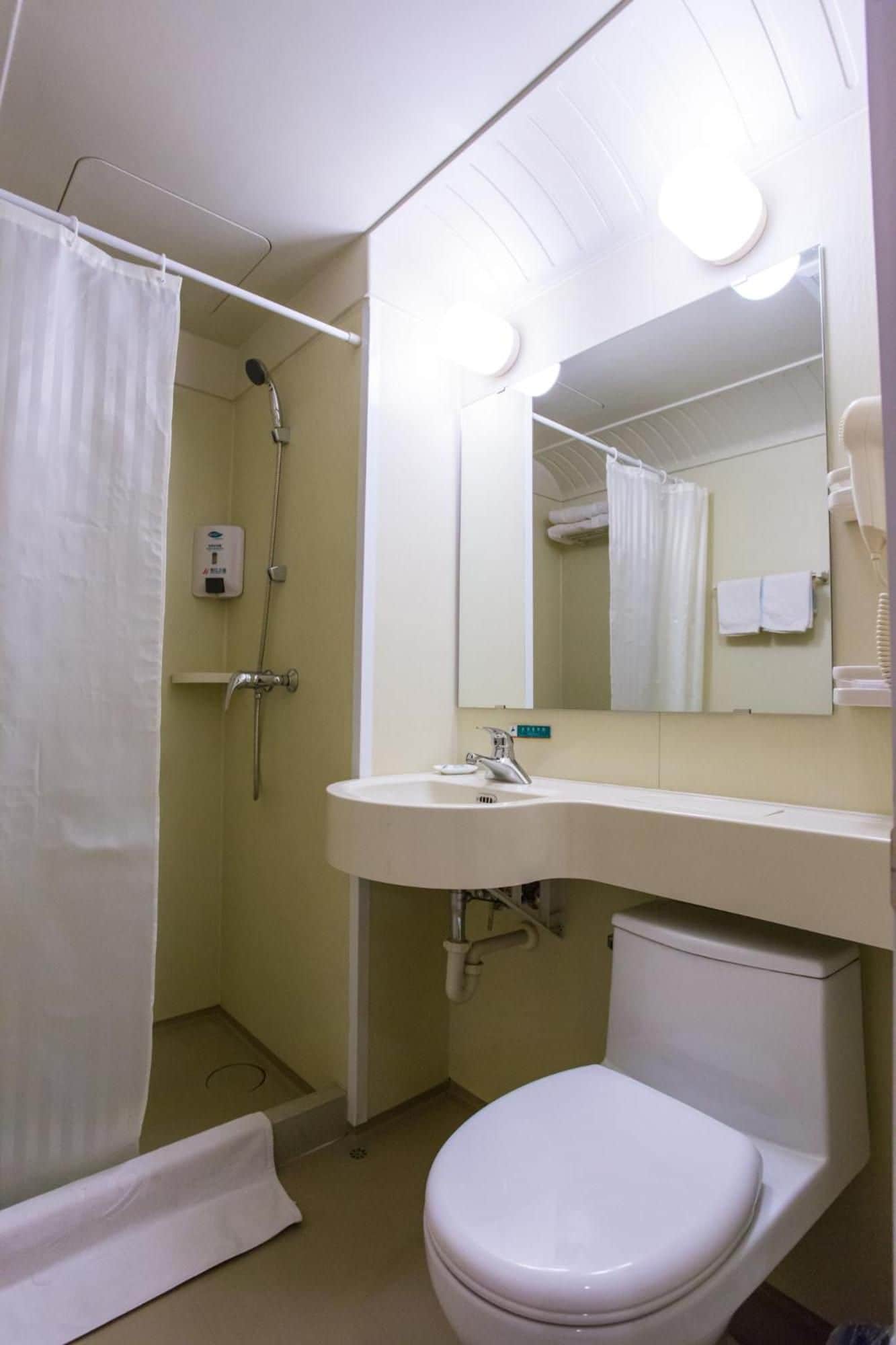 Et badeværelse med bruser, toilet, håndvask og spejl.