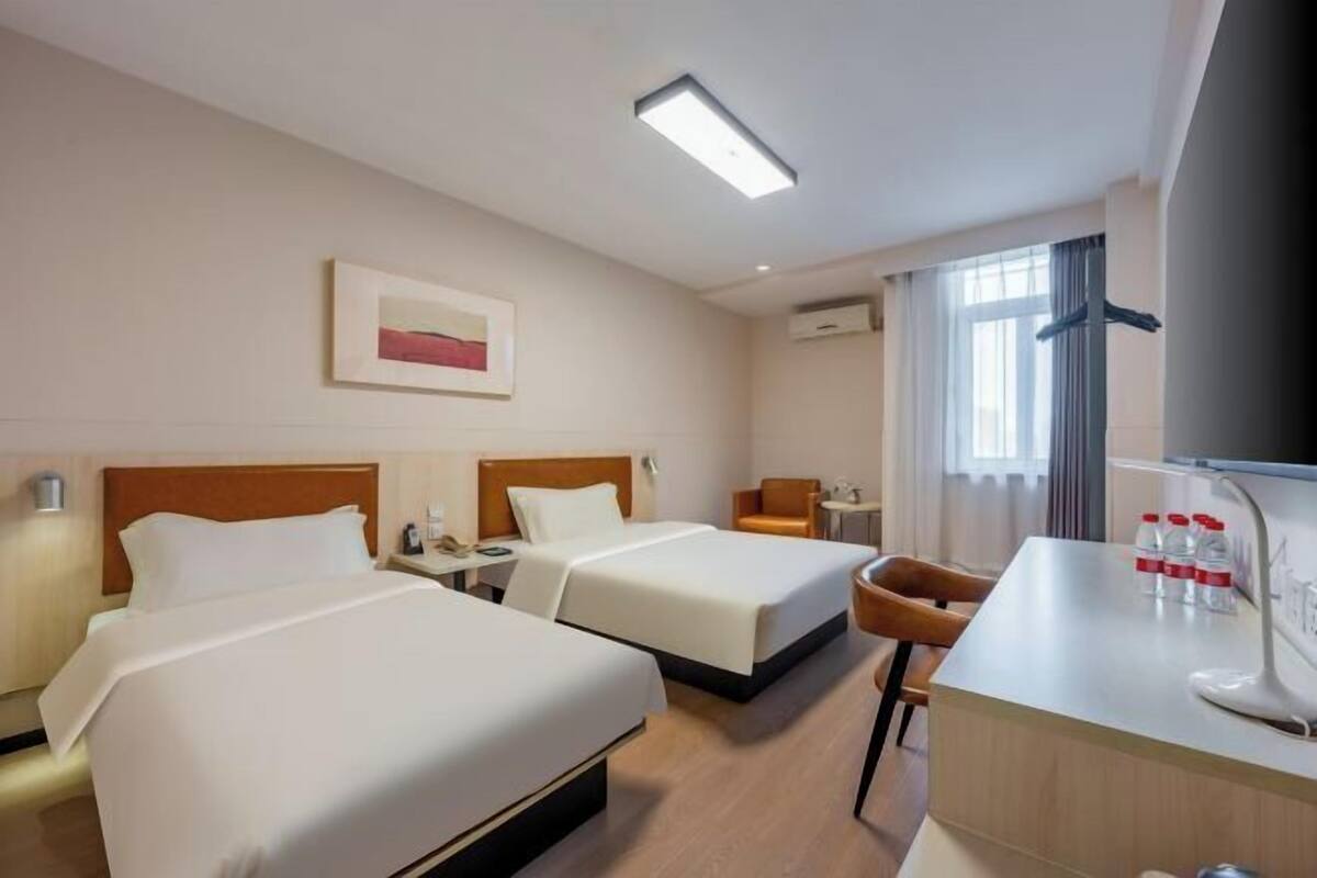A hotel room with two beds, a desk, a chair, a TV, and a window with curtains.