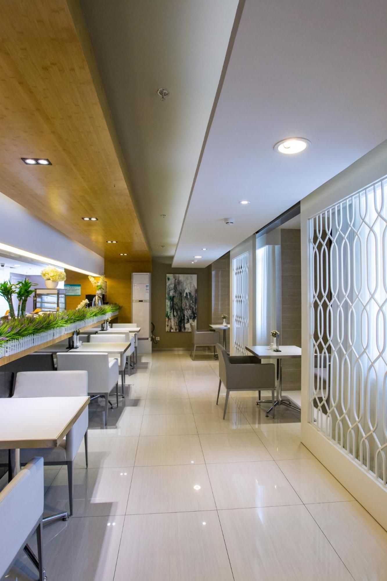 A modern interior with a long dining area, white tables, and chairs, a wooden ceiling, and a decorative white partition.