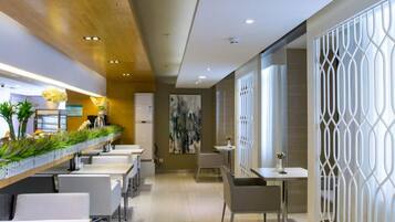 A modern interior with a long dining area, white tables, and chairs, a wooden ceiling, and a decorative white partition.