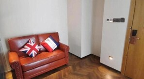 A room with a brown leather sofa, a door with a lock, and a herringbone-patterned wooden floor.