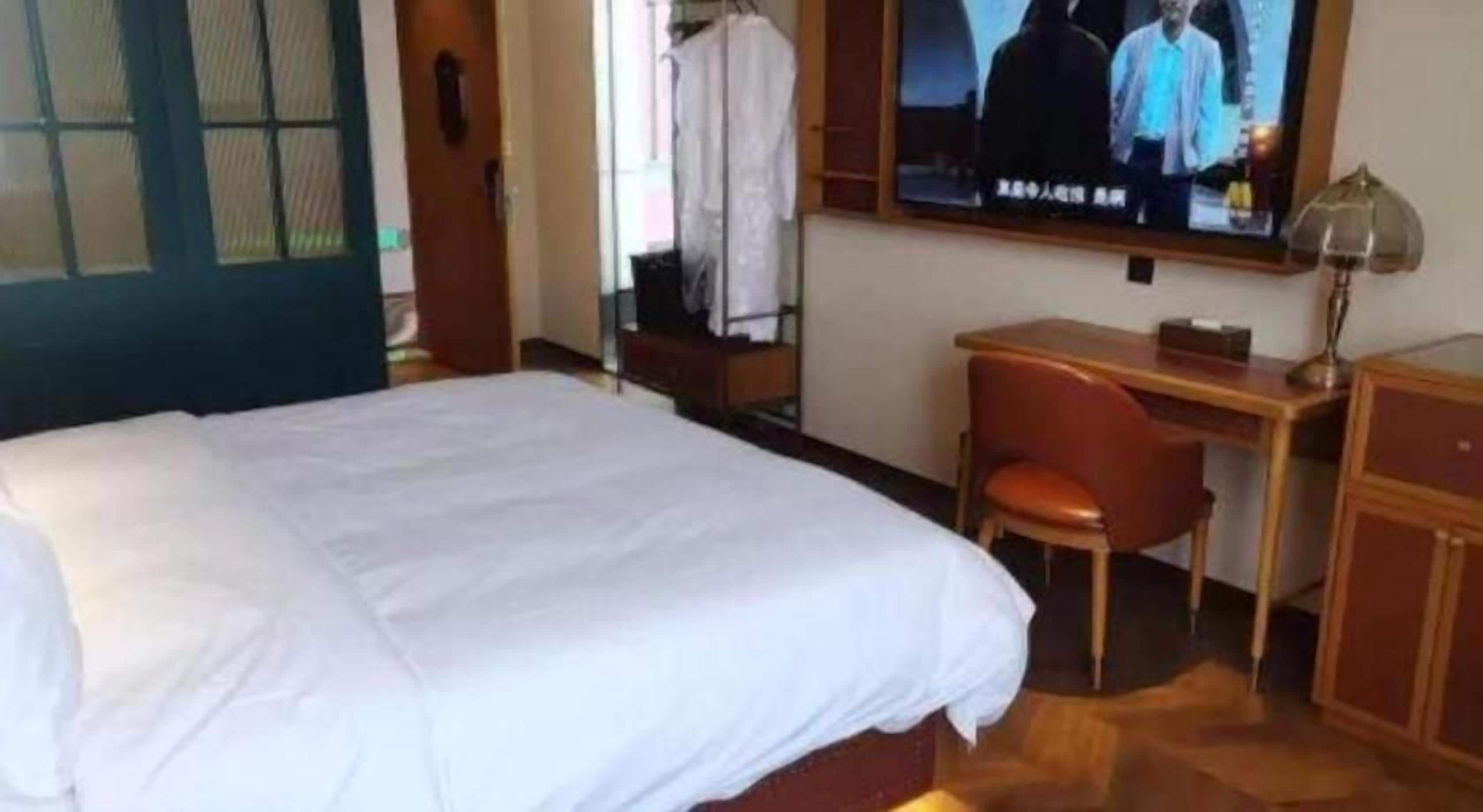 A hotel room with a bed, a desk, a chair, and a television.