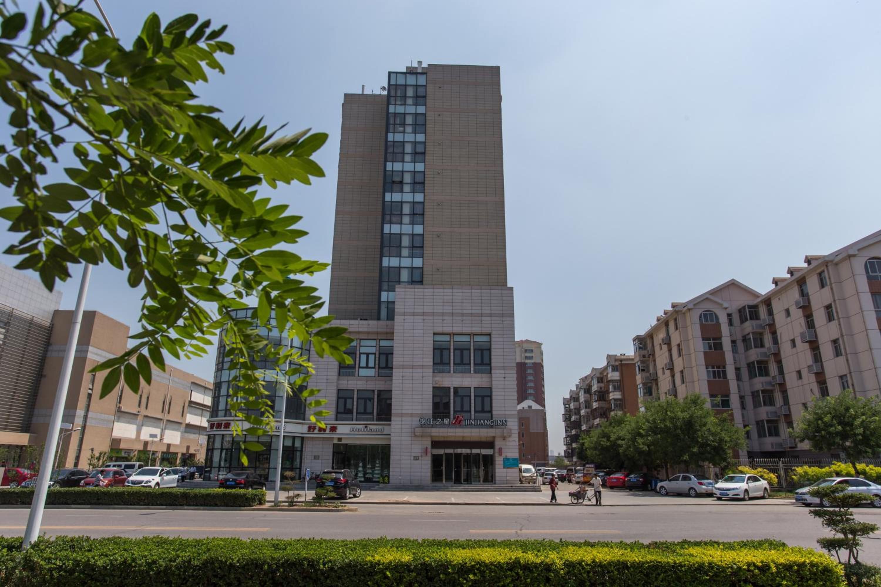 Un bâtiment moderne doté d’une entrée verticale imposante, entouré d’autres immeubles résidentiels et d’un espace de stationnement.