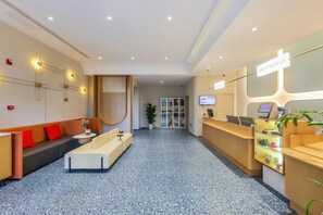 A hotel reception area with a sofa, a reception desk, a plant, and a television screen. - Jinjiang Inn (Tianjin South Railway Station) (Tianjin)