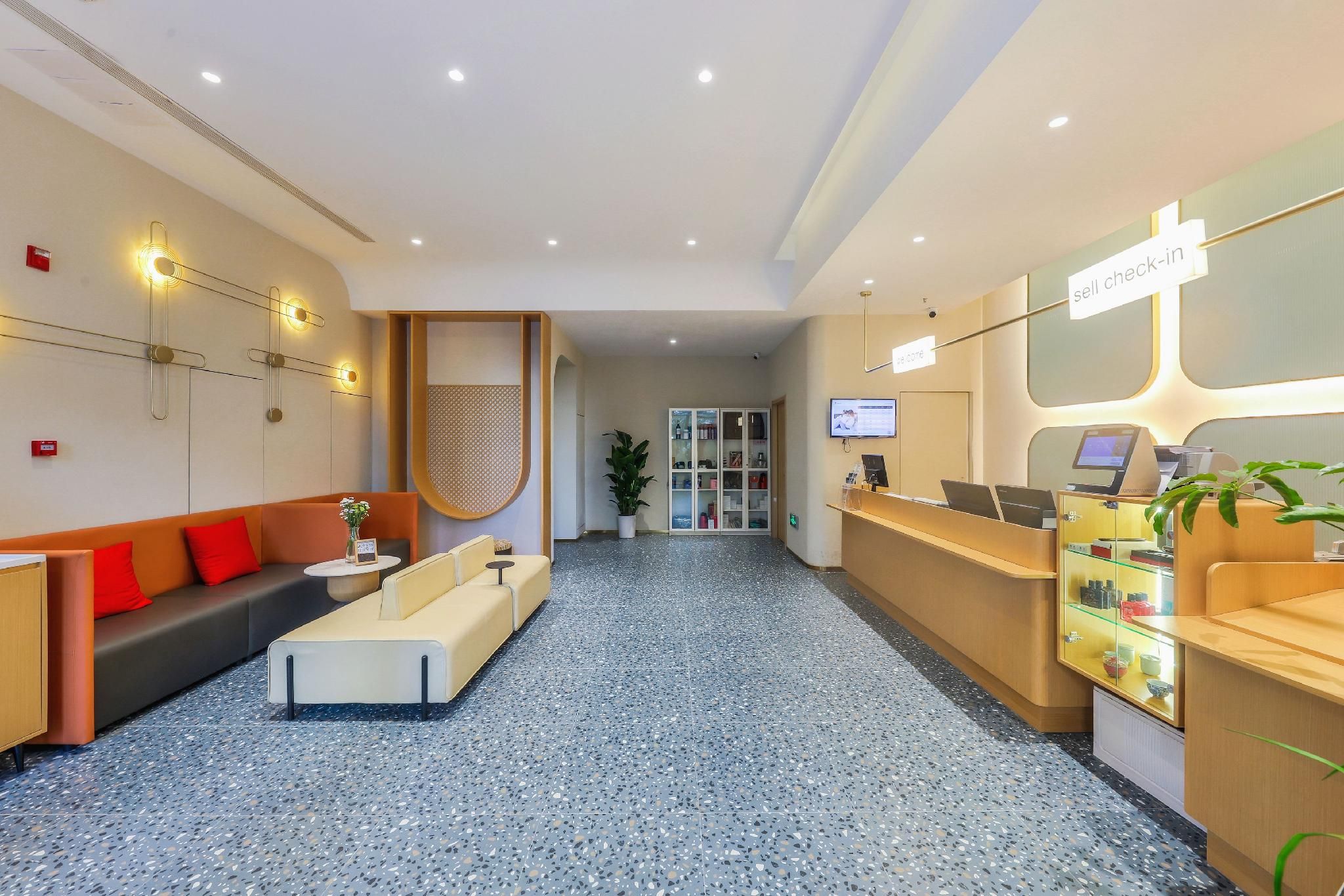 A hotel reception area with a sofa, a reception desk, a plant, and a television screen.