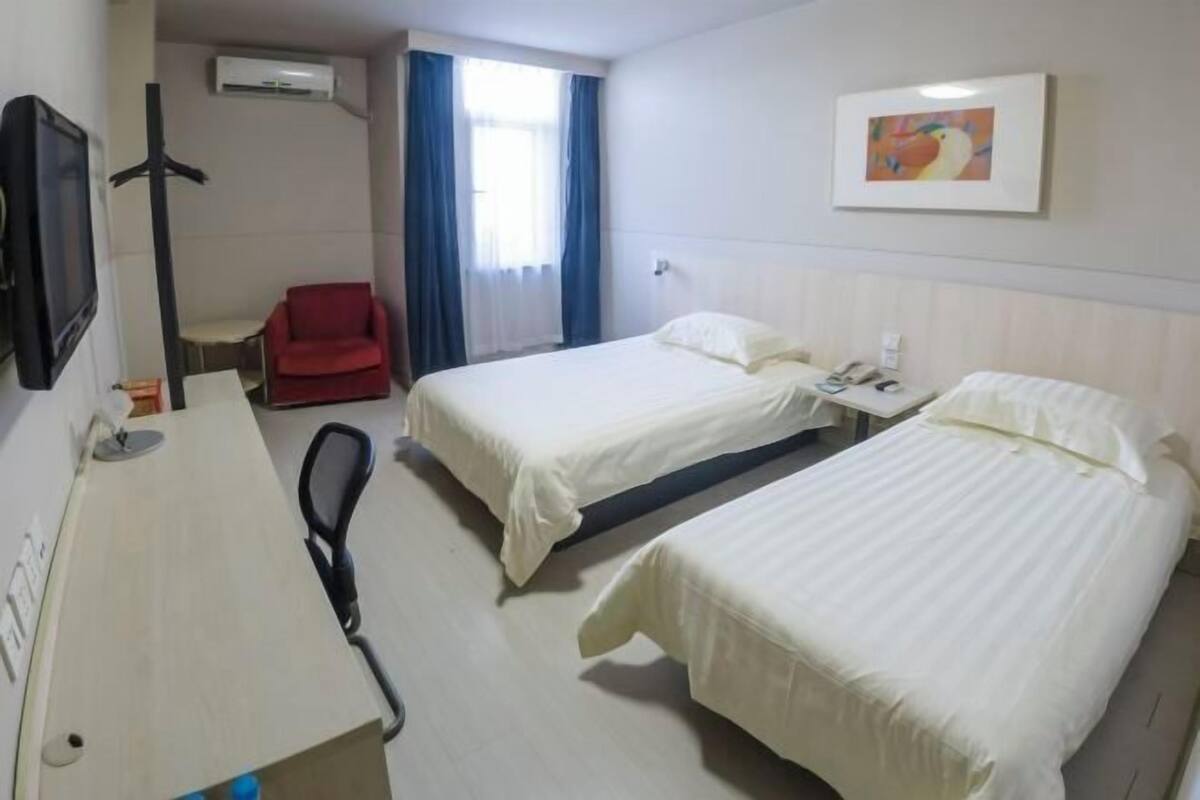 A hotel room with two beds, a desk with a telephone, a chair, and a television.