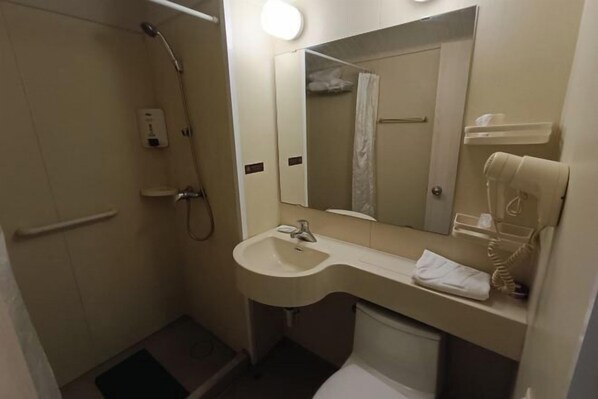 Un baño pequeño con ducha, lavamanos, espejo y barra para toallas.