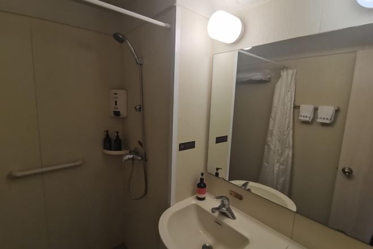 A bathroom with a sink, mirror, shower, and hand dryer.