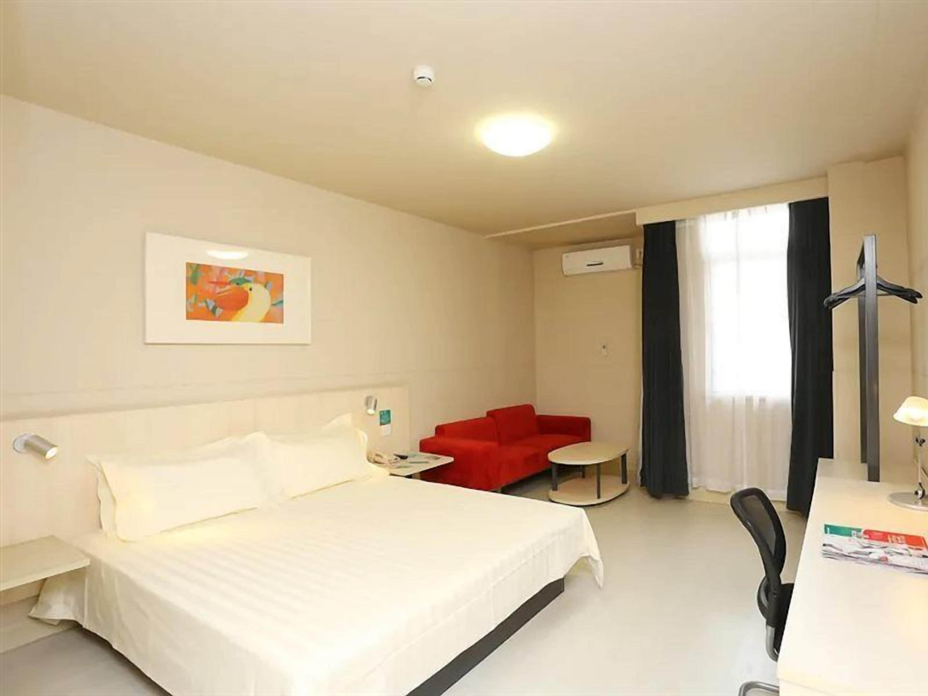 Quarto de hotel com cama, sofá vermelho, mesinha, escrivaninha e uma cadeira.