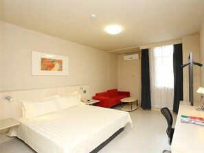 A hotel room with a bed, a red sofa, a small table, a desk, and a chair.