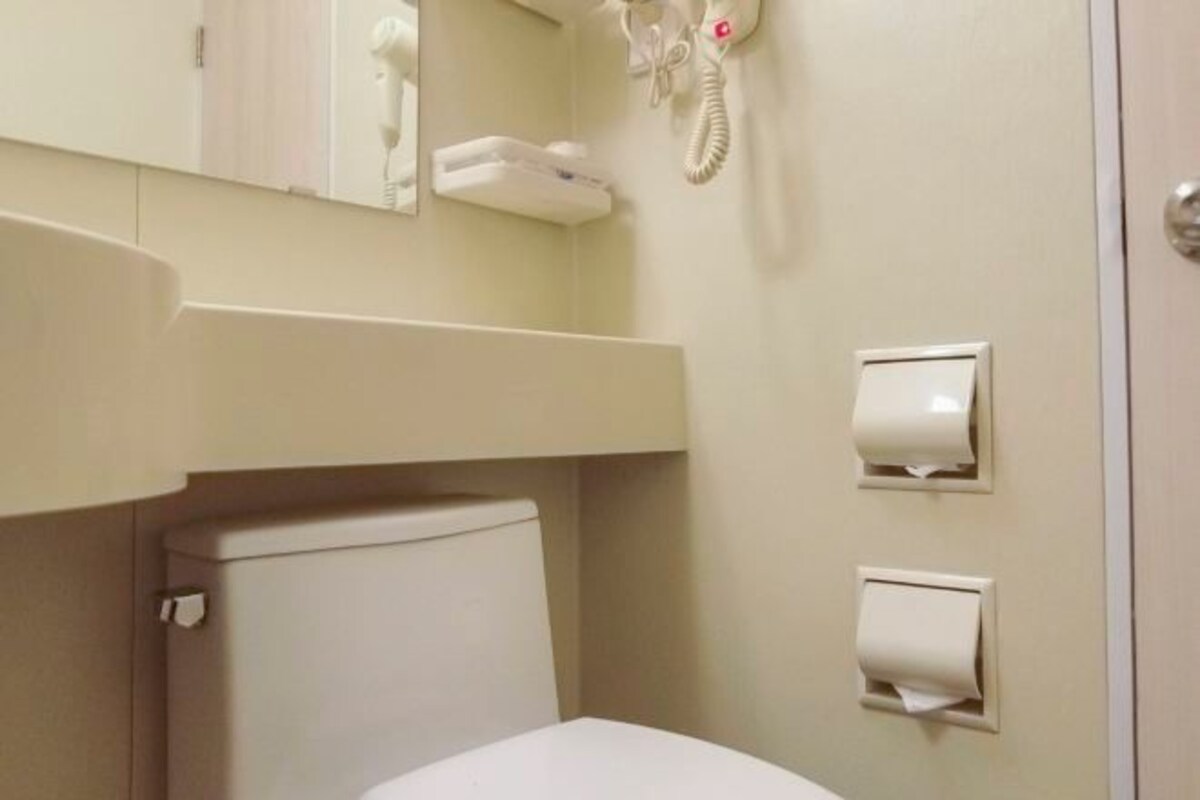 A bathroom with a toilet, a hand dryer, and a telephone mounted on the wall.