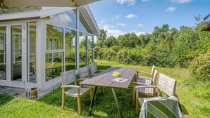 A patio with a table and chairs under a canopy, surrounded by a garden and a white building with glass doors. - Lovely home in ølsted with kitchen (Ølsted)