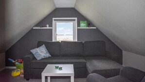 Ein gemütliches Dachzimmer mit einem grauen Sofa, einem kleinen weißen Tisch und einem Fenster mit Blick auf ein Gewässer.