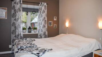 Ein Schlafzimmer mit einem Bett, einem Fenster mit Vorhängen, einem Nachttisch mit Lampe und einer Wand mit gerahmten Bildern.