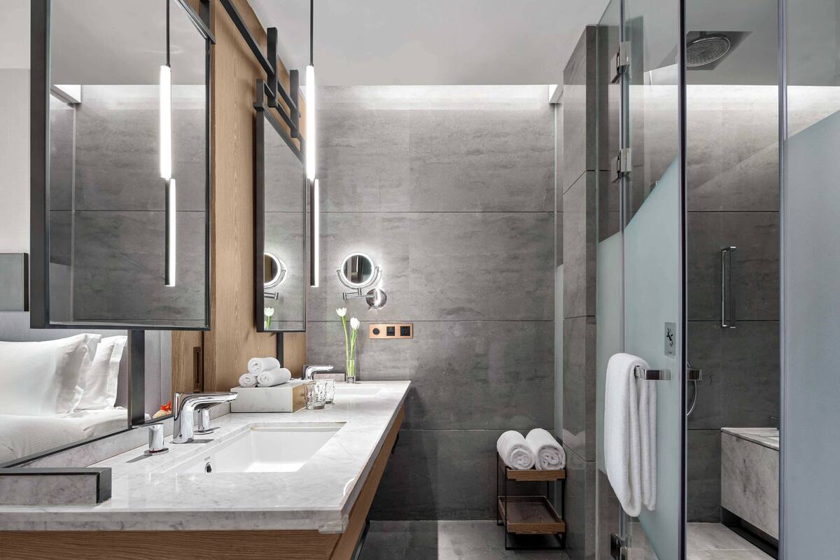 A modern bathroom with a large mirror, two sinks, a shower, and a towel rack.