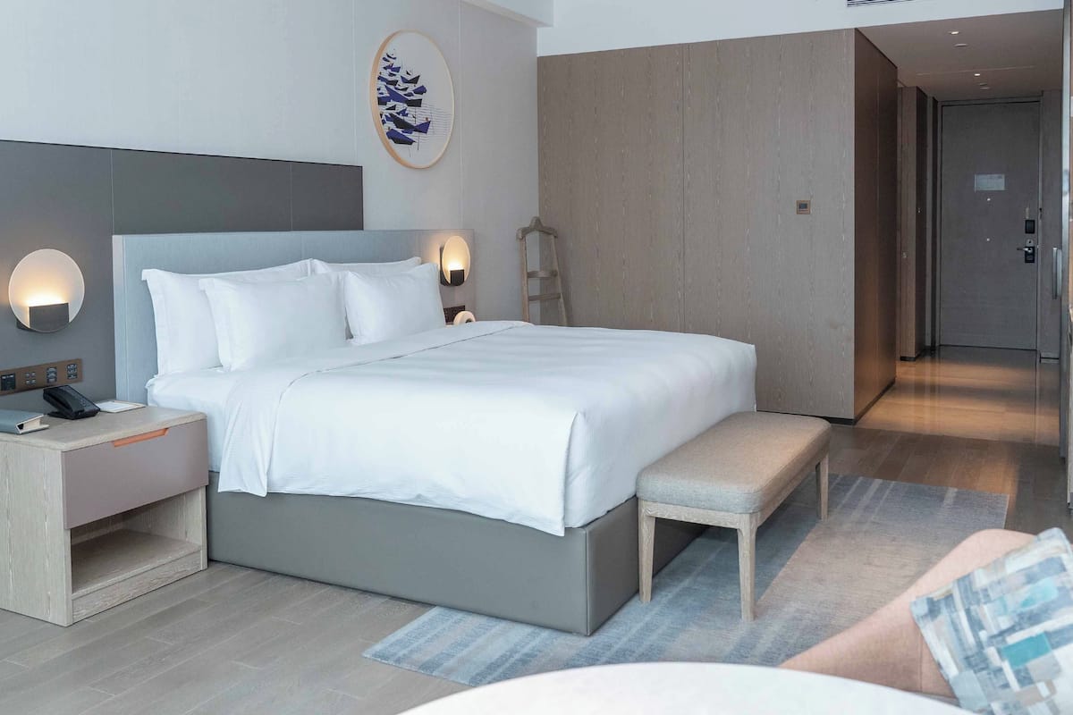 A modern hotel room with a large bed, bedside tables, a desk, and a bench.