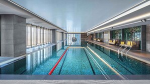 Piscina interior moderna con carriles delimitados, una plataforma de salto central y zonas de estar con cojines.