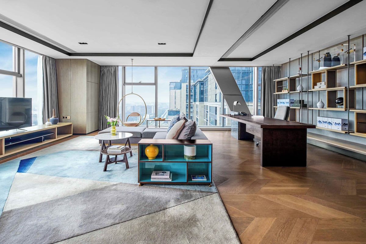 A modern living room with a large window, a sofa, a coffee table, and a bookshelf.
