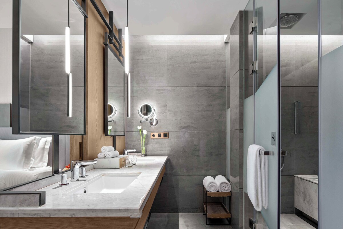 A modern bathroom with a large mirror, two sinks, a shower, and a towel rack.