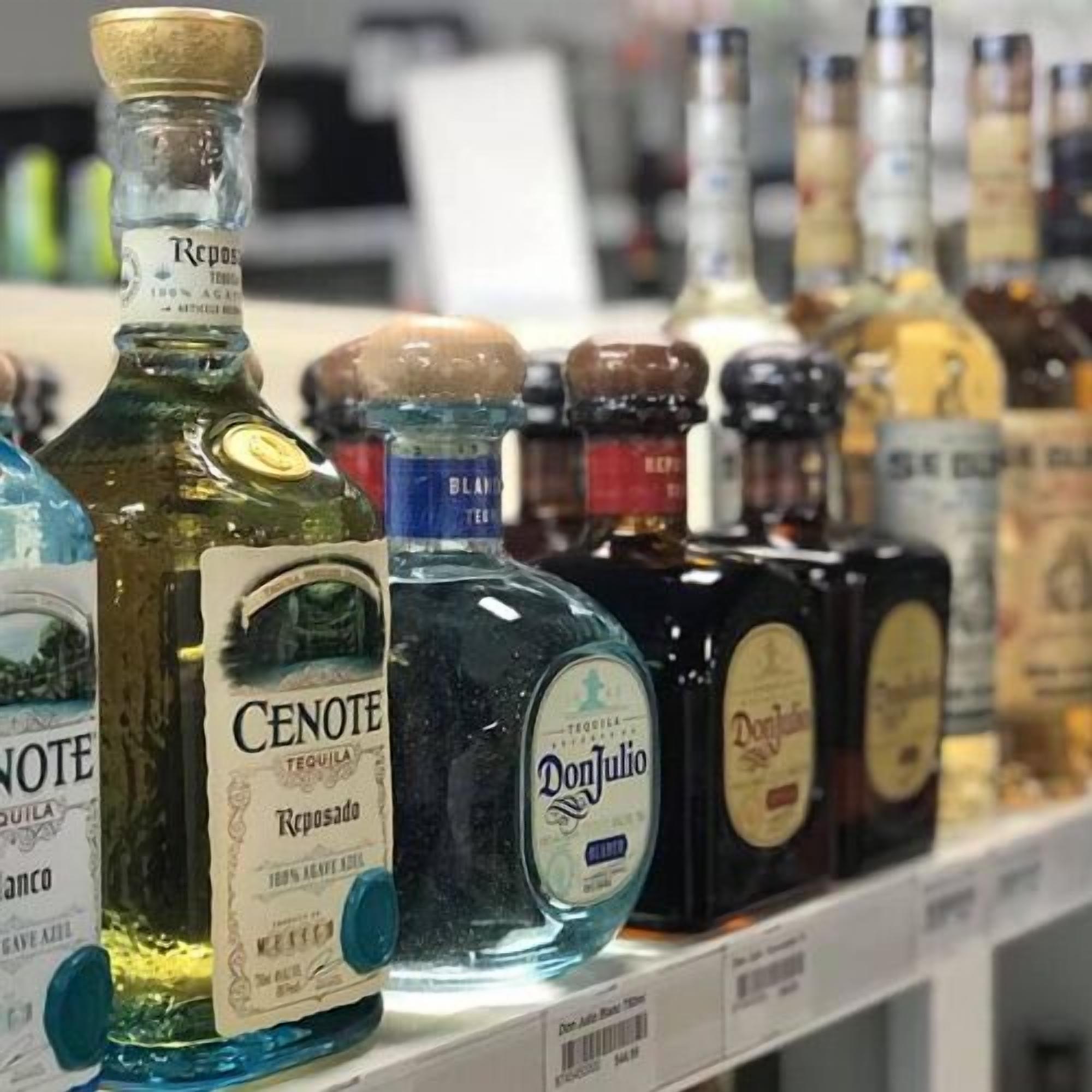 A shelf with various bottles of alcohol, including brands like Don Julio and CENOTE.