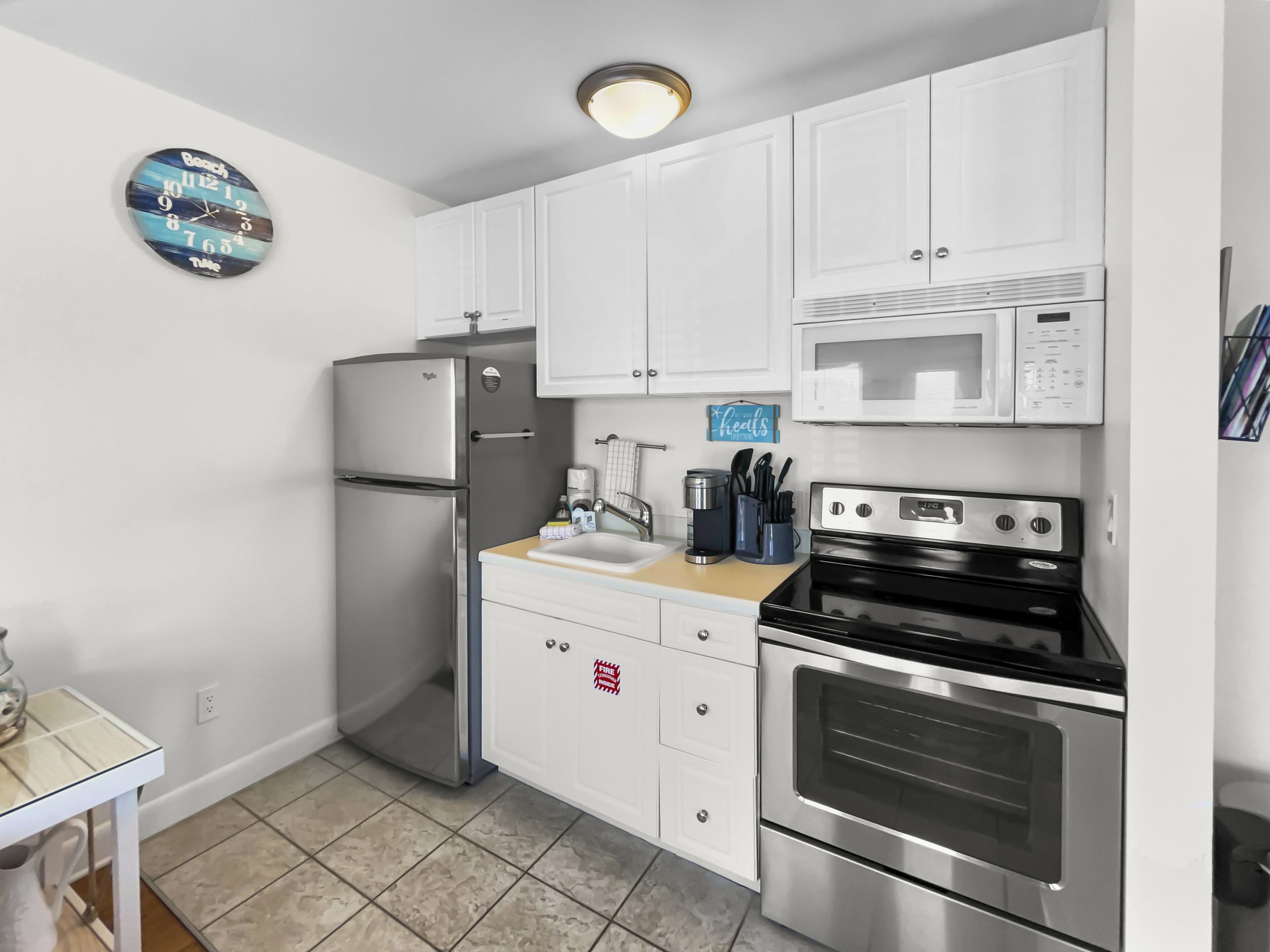 A compact kitchen with white cabinets, a stainless steel refrigerator, a microwave, and an oven.