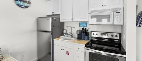 A compact kitchen with white cabinets, a stainless steel refrigerator, a microwave, and an oven.