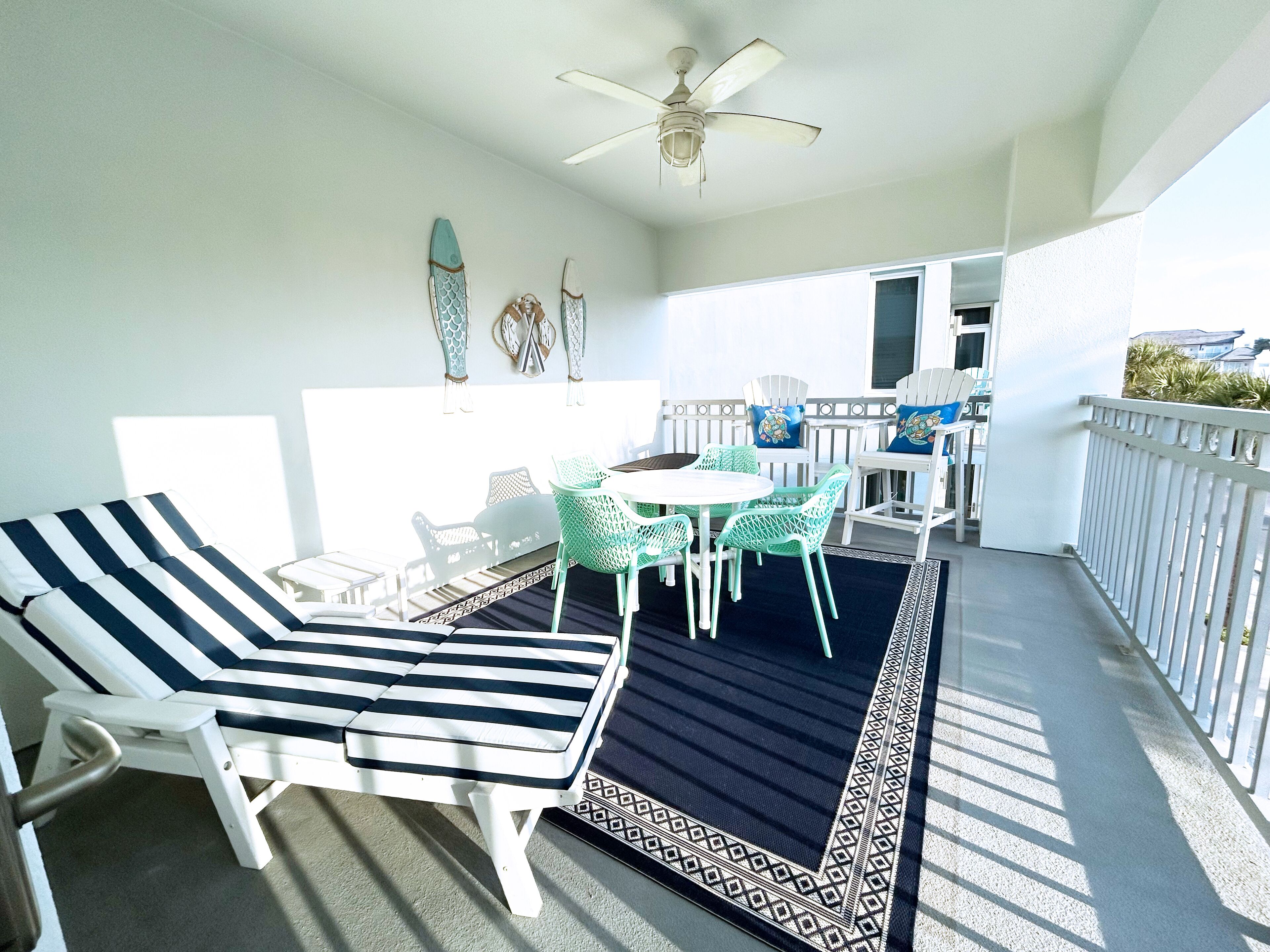 A balcony with a ceiling fan, a dining table with chairs, and a lounge chair.