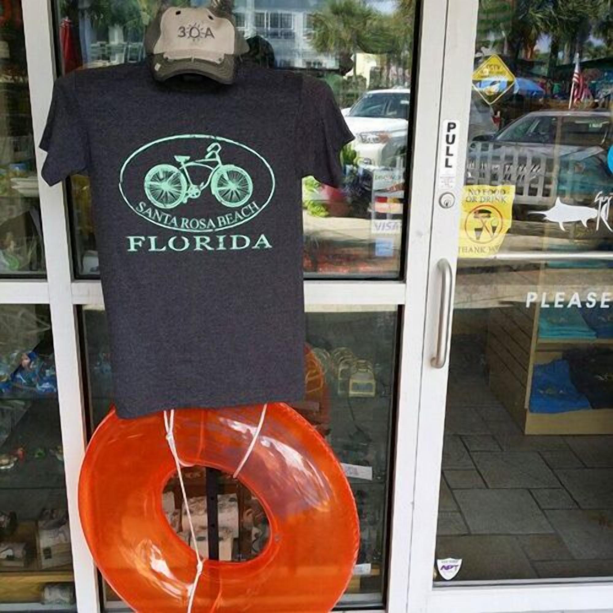 Vitrine com uma camiseta de tema de bicicleta pendurada na janela e um grande boi laranja.