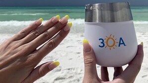 A person holding a sunscreen bottle with a beach and ocean in the background. - "Golden on 30A" | Gulf Views | Pool & hot tub | Tennis | Walk to Shops & Restaurants (Santa Rosa Beach)
