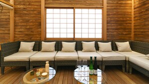 A wooden-paneled room with a sofa and a glass table with bottles and glasses. - KONJAKUSO Osaka Shinsaibashi "TARUKAISEN" Rooftop SPA (Osaka)