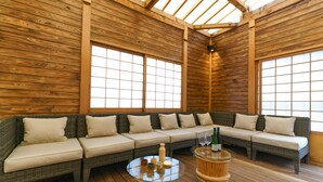 A wooden interior with a long sofa, a glass table with bottles, and a wooden barrel. - KONJAKUSO Osaka Shinsaibashi "TARUKAISEN" Rooftop SPA (Osaka)